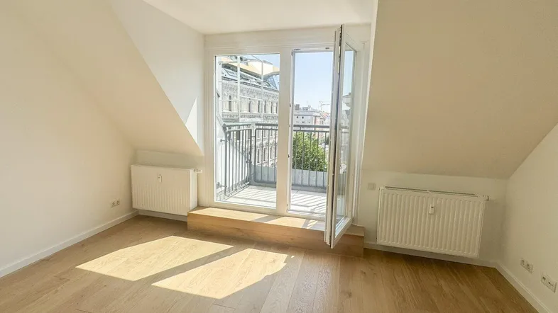Helles Zimmer im Dachgeschoss mit Holzboden und Zugang zu einem französischen Balkon.