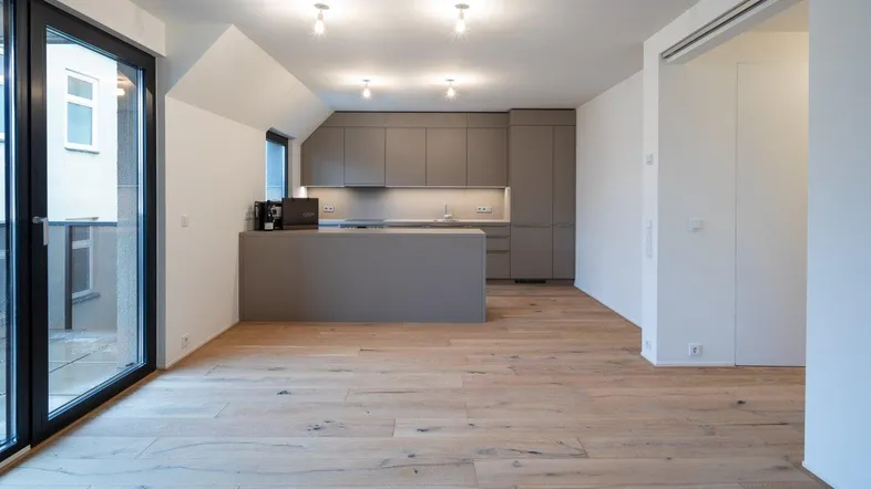 Heller offener Wohnbereich mit moderner Küche, Holzboden und Zugang zum Balkon.
