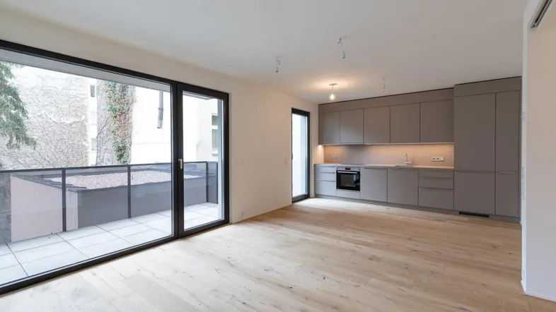 Heller offener Wohnbereich mit moderner grauer Einbauküche, Holzboden und Zugang zu einer Terrasse.