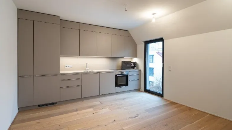 Moderne Küchenzeile mit hellen Schränken, Holzboden, Dachschräge und Zugang zu einem Balkon.