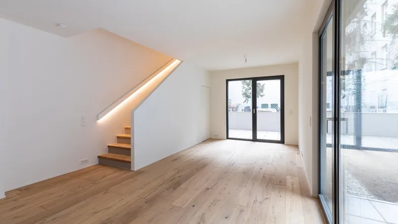Helles, modernes Wohnzimmer mit Holzboden, integrierter Treppenbeleuchtung und Zugang zur Terrasse.