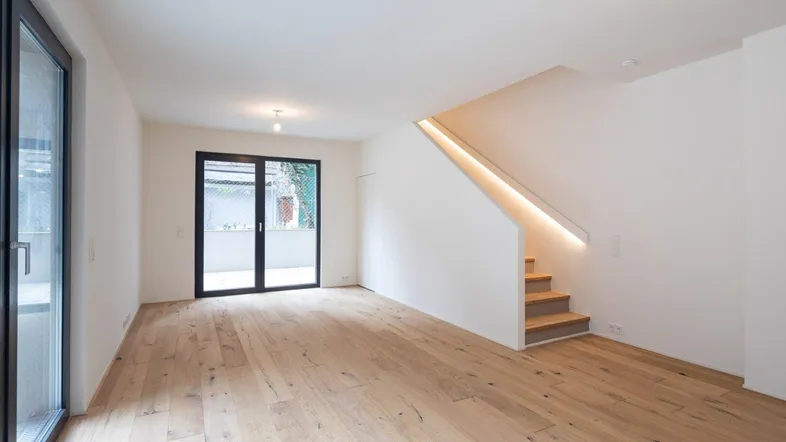 Helles, offenes Wohnzimmer mit Holzboden und moderner Treppe mit integrierter Beleuchtung.