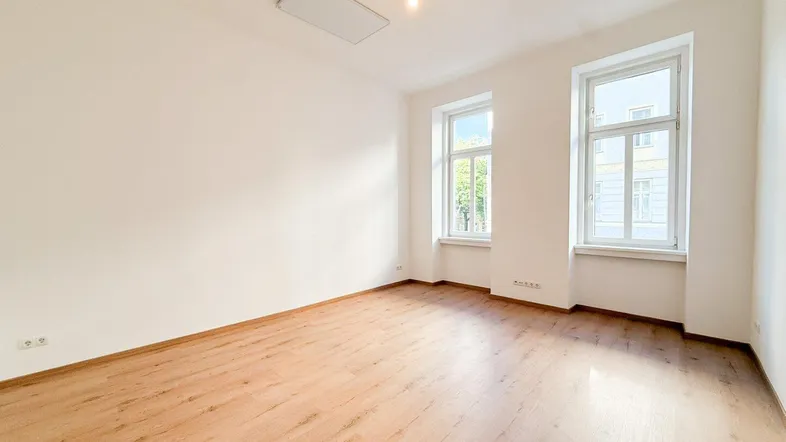 Heller, leerer Raum mit Laminatboden und zwei großen Fenstern, ideal als Wohn- oder Schlafzimmer.