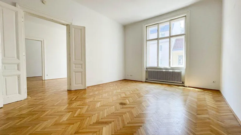 Helles Wohnzimmer mit Fischgrätparkettboden und hohen Flügeltüren, die zu weiteren Räumen führen.