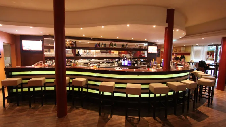Eine moderne Bar mit beleuchteter Theke, bequemen Barhockern und Holzboden, ideal für gesellige Abende.