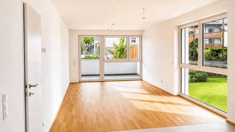 Helles, leeres Zimmer mit Parkettboden, großen Fenstern und Balkonzugang.