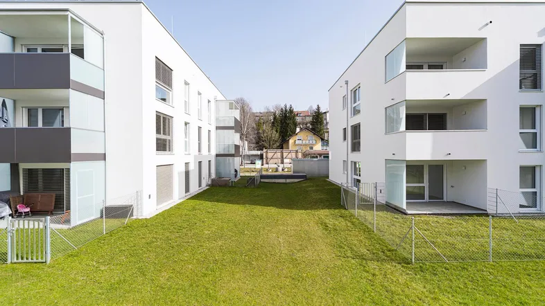 Moderne Wohngebäude mit weißer Fassade und einem gepflegten Gemeinschaftsgarten in sonniger Lage.