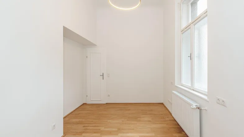 Heller, leerer Raum mit hohen Decken, Parkettboden und einem großen Fenster.