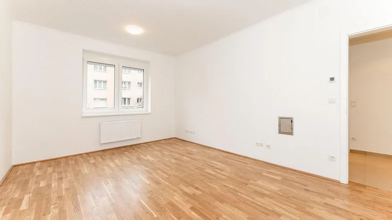 Geräumiges Zimmer mit hellem Parkettboden und Blick auf die umliegenden Gebäude.