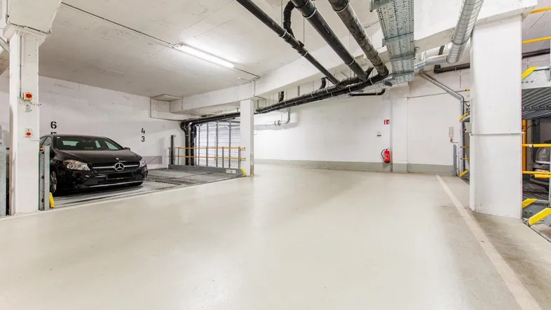 Geräumige und gut beleuchtete Tiefgarage mit Betonboden und modernen Installationen.