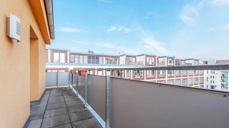 Geräumige Dachterrasse mit Fliesenboden und Blick auf umliegende Gebäude unter blauem Himmel.