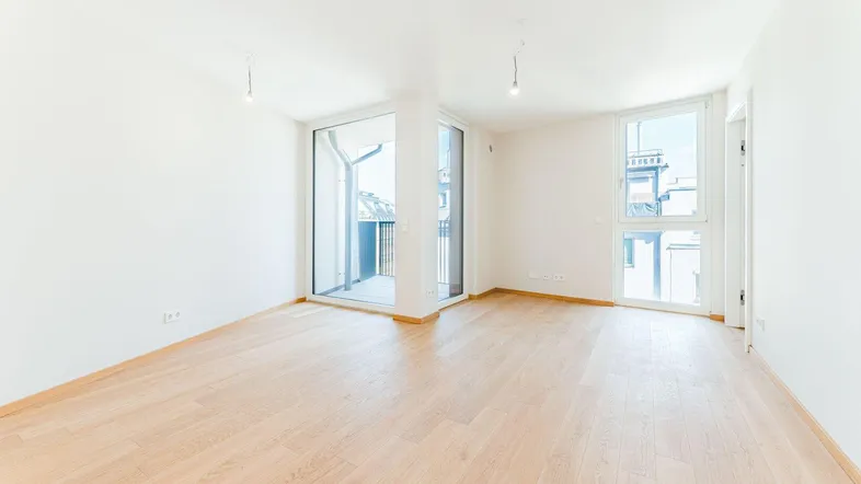 Helles, leeres Zimmer mit Parkettboden und Zugang zu einem Balkon, bereit zur Einrichtung.