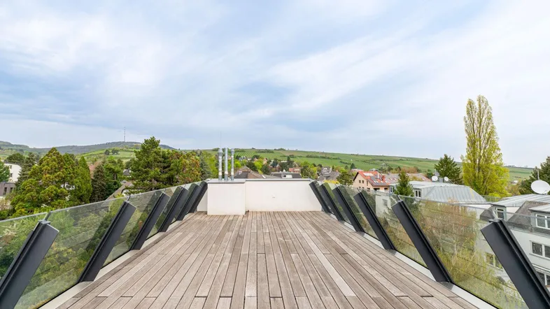 Geräumige Dachterrasse mit Holzbelag und Glasgeländer, bietet einen weiten Blick ins Grüne.