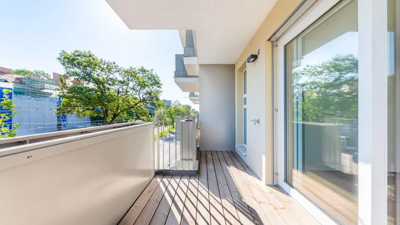 Heller Balkon mit Holzboden und Blick auf die grüne Umgebung und die Straße.