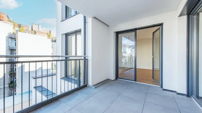 Heller Balkon mit Fliesenboden und Blick in den leeren Innenraum der Wohnung.