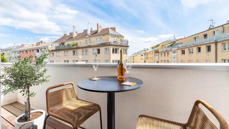 Möblierter Balkon mit Holzboden und Blick auf die umliegenden Gebäude und den Himmel.