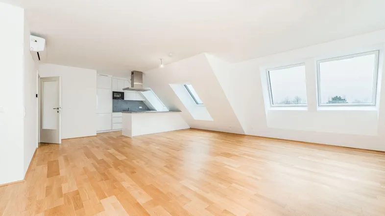 Helles, offenes Wohn-Esszimmer mit Holzboden, Dachschrägen und integrierter Küche.