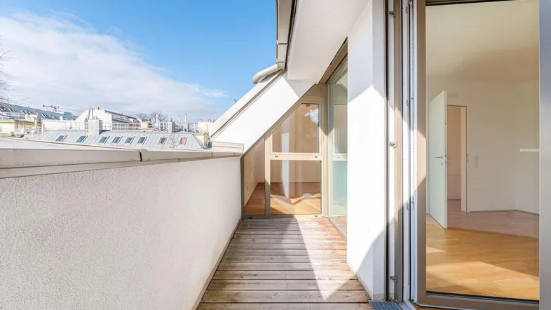 Heller Balkon mit Holzboden und Blick auf die umliegenden Dächer und den Himmel.