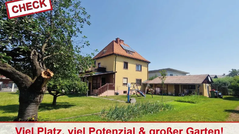 Großer Garten mit viel Grünfläche, Bäumen und einem kleinen Spielplatz vor dem gelben Haus.