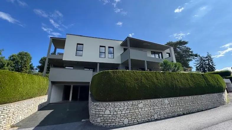 Moderne Wohnanlage mit klaren Linien und gepflegter Hecke unter blauem Himmel.