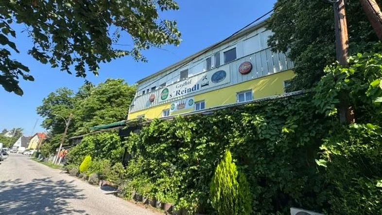 Ansicht des Gasthofs Reindl von der Straße aus, umgeben von üppigem Grün und Bäumen.