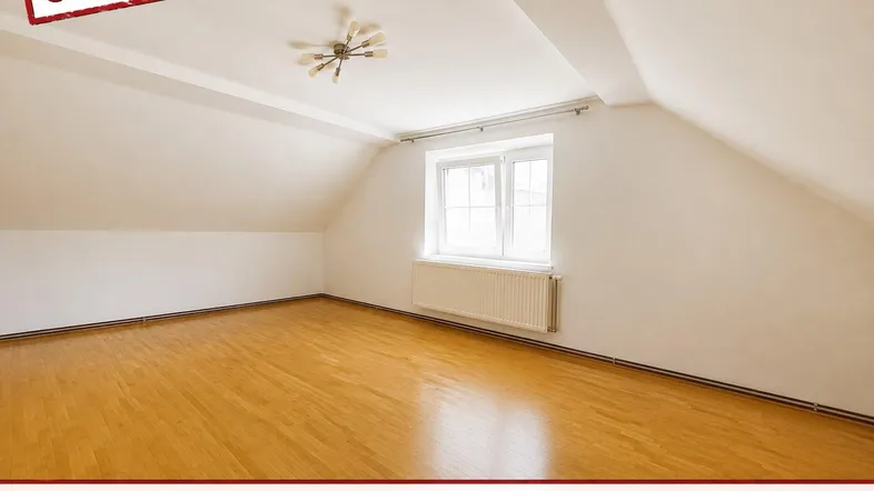 Helles Zimmer mit Dachschrägen, Holzfußboden und einem Fenster, das viel Tageslicht hereinlässt.