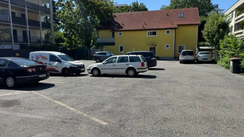 Gelbes Gebäude mit rotem Dach und angrenzendem Parkplatz unter blauem Himmel an einem sonnigen Tag.