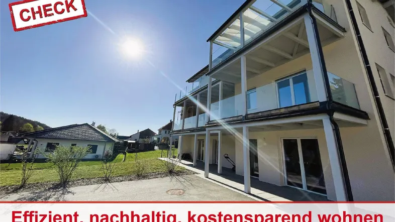 Modernes Mehrfamilienhaus mit Balkonen und viel Sonnenlicht in ländlicher Umgebung.