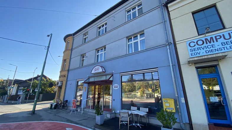Gebäudeansicht mit blauer Fassade, großen Fenstern und einem kleinen Außenbereich vor dem Eingang.