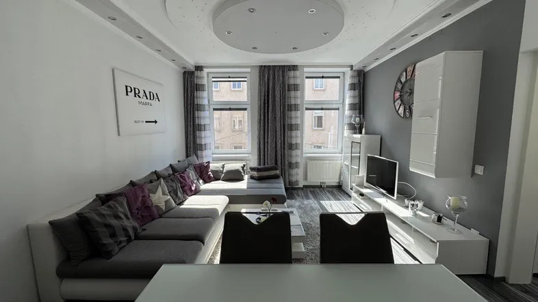 Helles Wohn- und Esszimmer mit moderner Einrichtung, L-förmigem Sofa und dekorativer Deckenbeleuchtung.