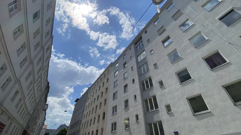 Mehrstöckiges Wohngebäude mit zahlreichen Fenstern und sonnigem Himmel, von der Straße aus gesehen.