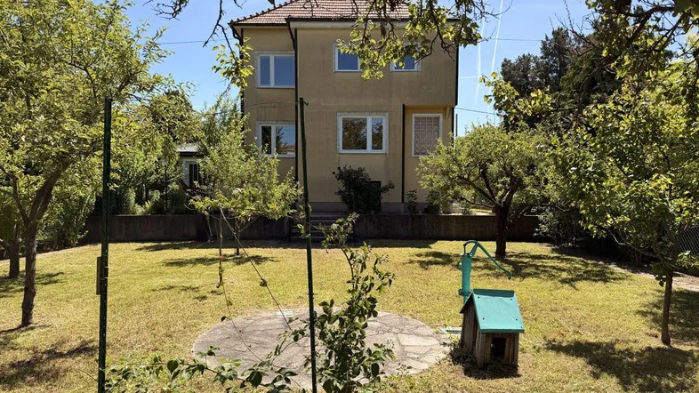 Großer Garten mit Rasenfläche und Obstbäumen hinter dem gelben Einfamilienhaus.