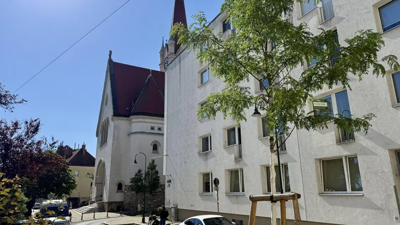 Straßenszene mit einem modernen Wohngebäude und einer historischen Kirche unter blauem Himmel.