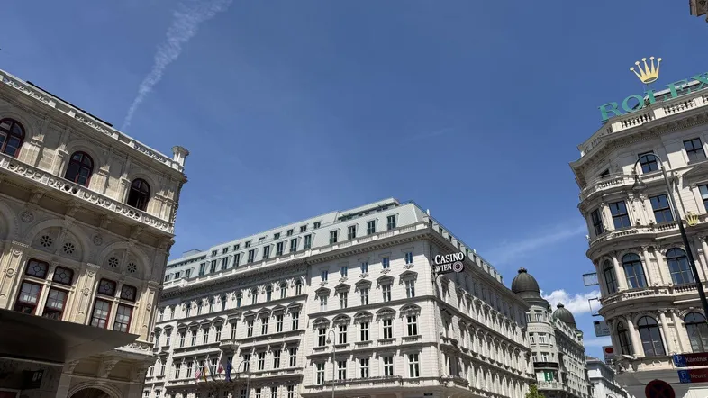Historische Gebäude in einer belebten Stadtstraße unter blauem Himmel mit Geschäften und Restaurants.