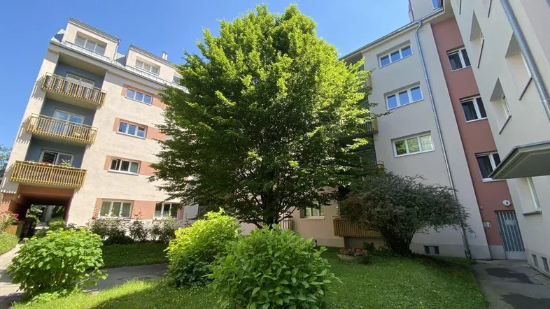 Mehrfamilienhaus mit begrüntem Innenhof und moderner Architektur unter blauem Himmel.