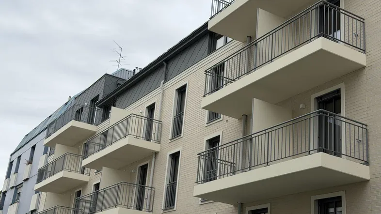 Neubau-Fassade mit modernen Balkonen und hellen Ziegeln unter bewölktem Himmel.