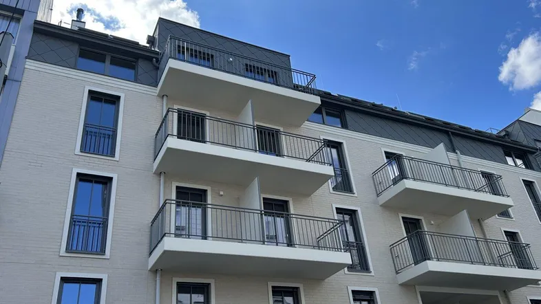 Moderne Wohnhausfassade mit mehreren Balkonen unter blauem Himmel und großen Fenstern.