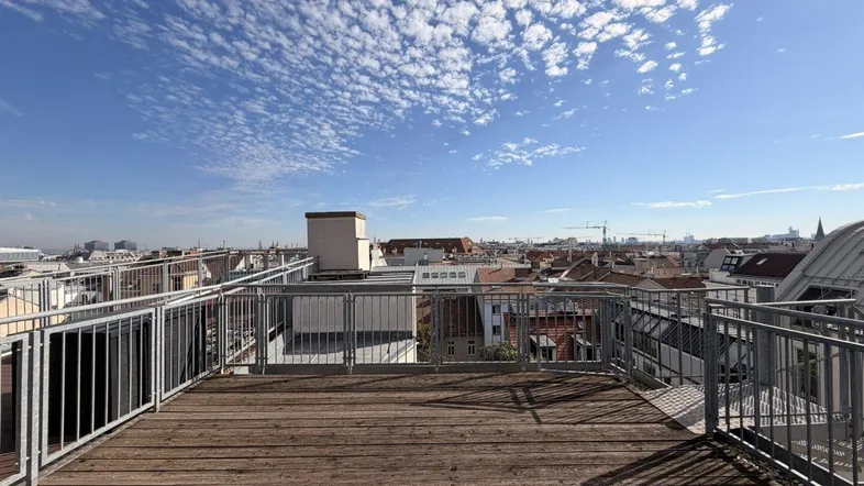 Große Dachterrasse mit Holzboden und weitem Blick über die Stadt unter blauem Himmel.