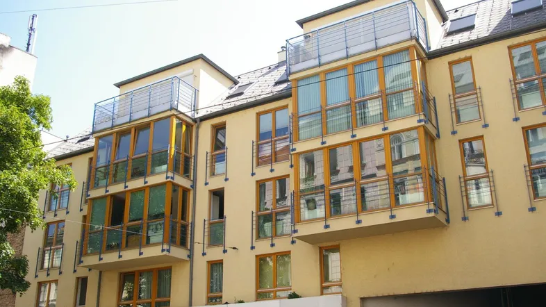 Modernes Mehrfamilienhaus mit großen Fenstern, Balkonen und Dachterrassen in städtischer Umgebung.