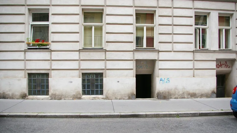 Fassade eines alten Gebäudes mit mehreren Fenstern und einem Eingangsbereich auf Straßenniveau.