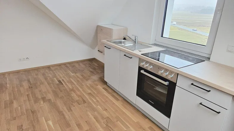 Kleine Einbauküche mit Kochfeld und Backofen in einem Raum mit Dachschrägen und Holzboden.