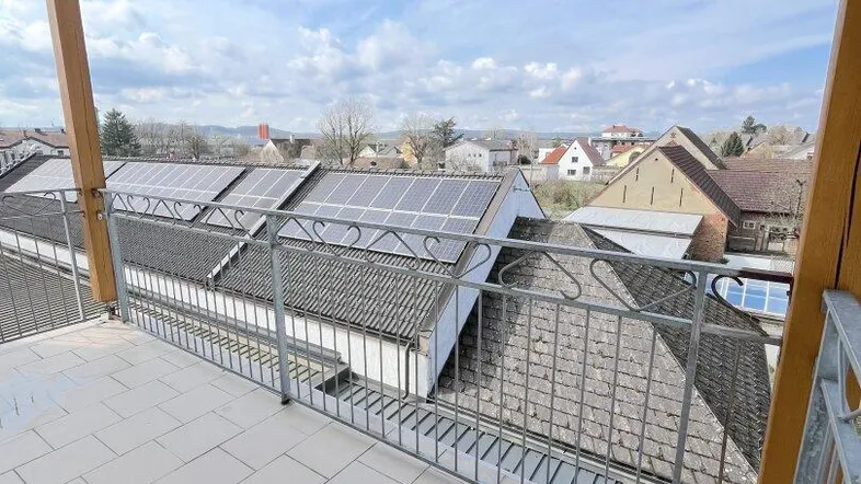 Geräumiger Balkon mit Fliesenboden, Metallgeländer und weitem Blick über die Dächer mit Solaranlagen.