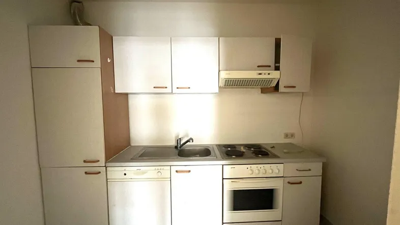 Kleine Einbauküche mit weißen Schränken, Spüle, Herd und integriertem Geschirrspüler.