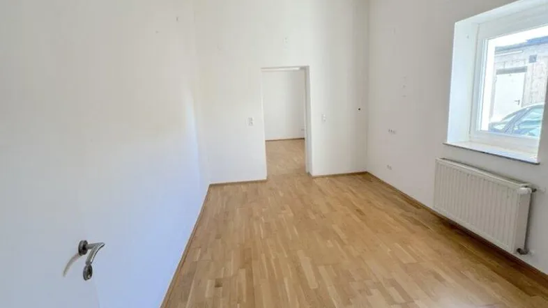 Helles Zimmer mit Holzboden, weißen Wänden und einem Fenster für natürliches Licht.