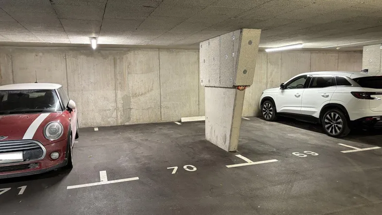 Tiefgarage mit markierten Parkplätzen und Betonwänden, beleuchtet von Deckenleuchten.