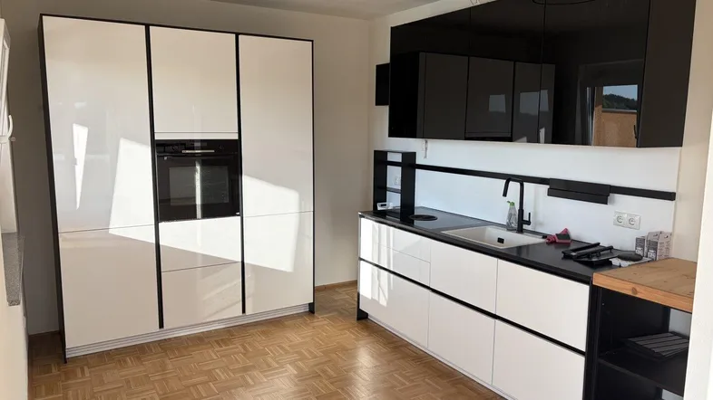 Moderne Küche mit weißen Hochglanzfronten, schwarzer Arbeitsplatte und integriertem Backofen.