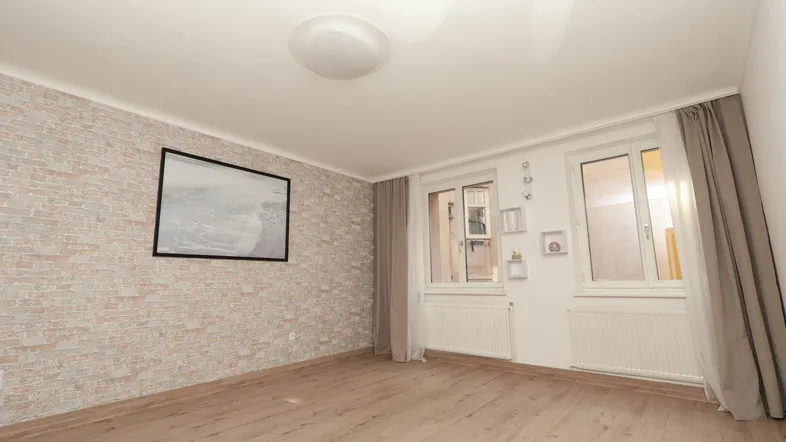 Helles Zimmer mit Laminatboden und dekorativer Ziegelwand, ideal als Wohn- oder Schlafzimmer.