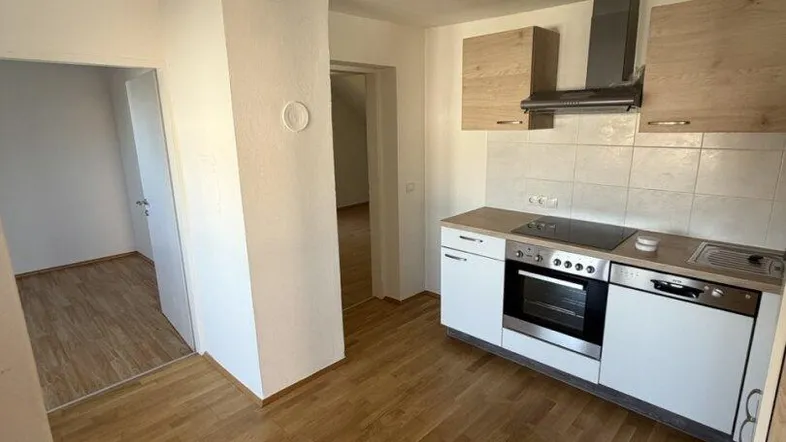 Offene Küche mit Holzschränken, integriertem Herd und Spüle, sowie hellem Parkettboden.