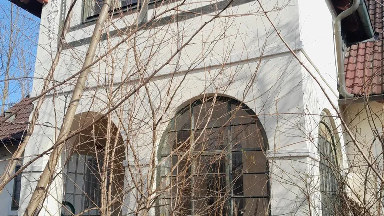 Nahaufnahme der Fassade eines älteren Gebäudes mit markanten Rundbogenfenstern und Dachziegeln.