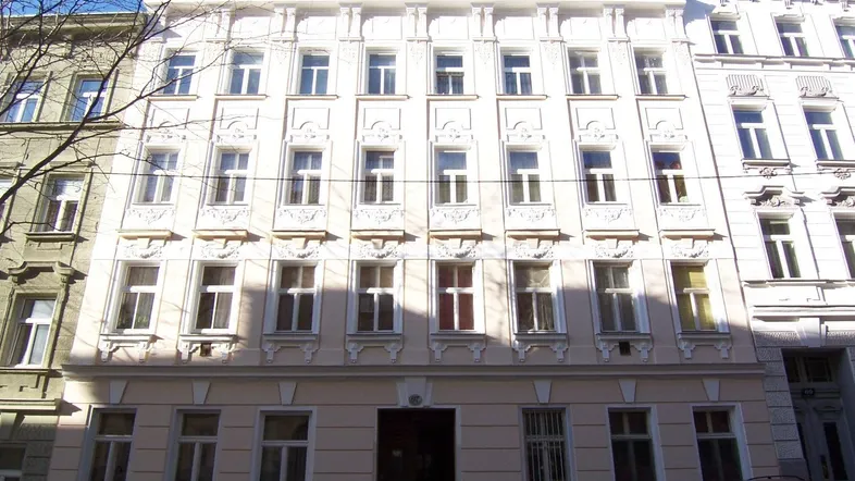Klassisches Mehrfamilienhaus mit einer gut erhaltenen, hellen Fassade und dekorativen Elementen in städtischer Umgebung.